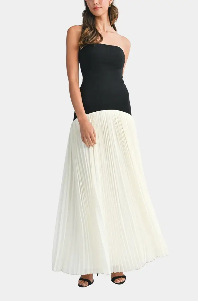 A woman wearing a strapless black and white pleated maxi dress, standing with one hand on her hip.