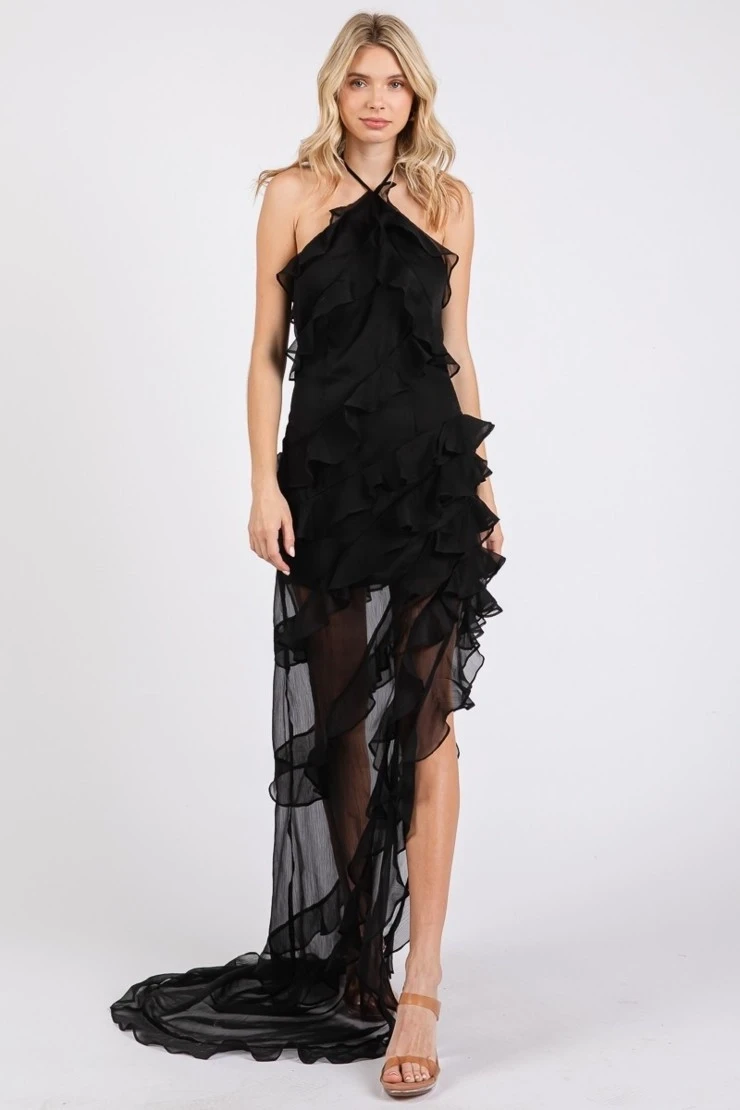A woman wearing a strapless black dress with ruffled details and a high slit, posing against a plain background.