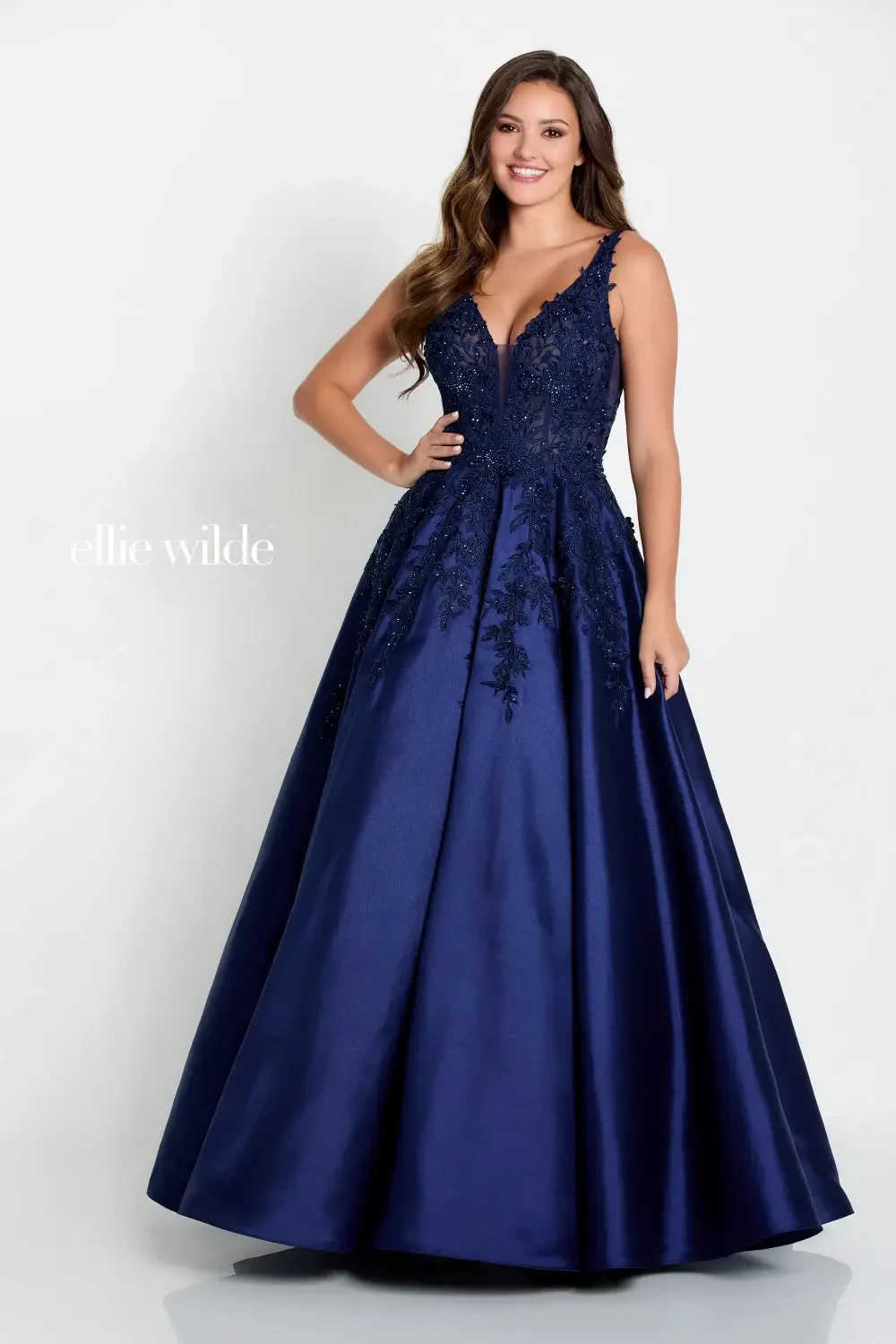 A woman in a navy blue ball gown with intricate beading and a fitted bodice, posing confidently against a white background.