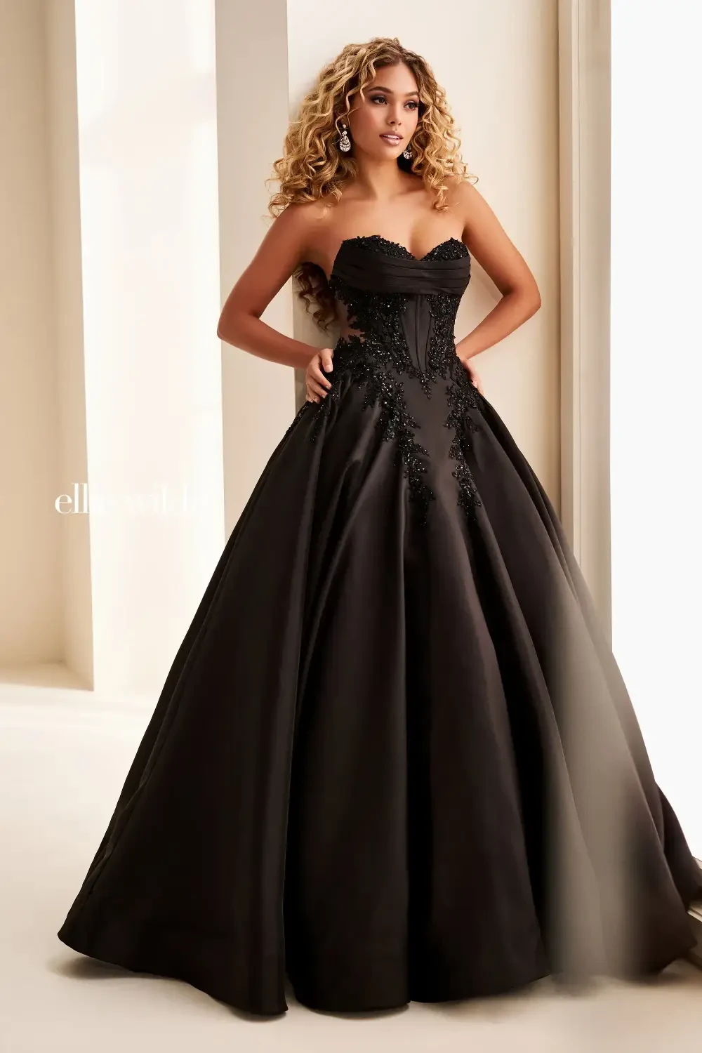 A person wearing a strapless black gown with a fitted bodice and a full skirt, standing in a bright indoor setting.